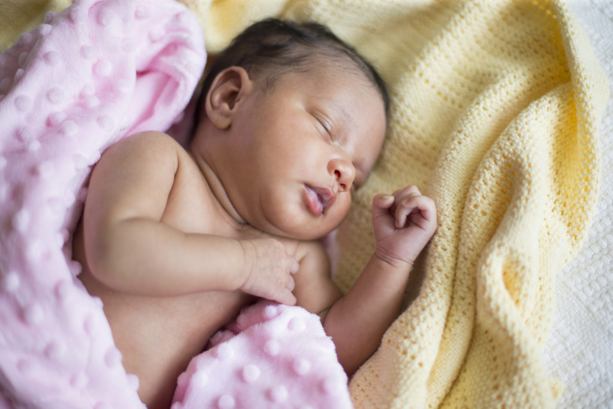 一个睡在床上的新生女婴，裹着一条粉红色的毯子。