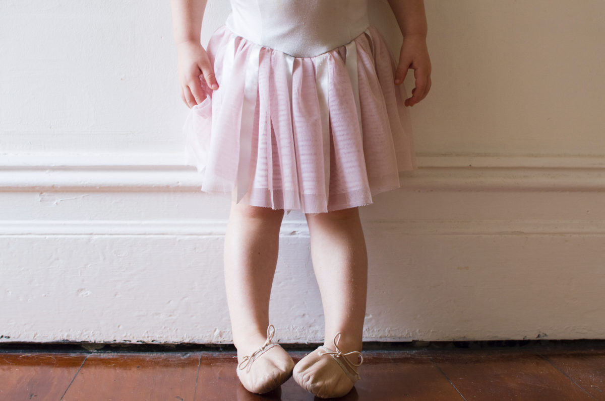 穿着粉色短裙和芭蕾舞鞋的蹒跚学步的孩子站在老式的走廊上(裁剪)