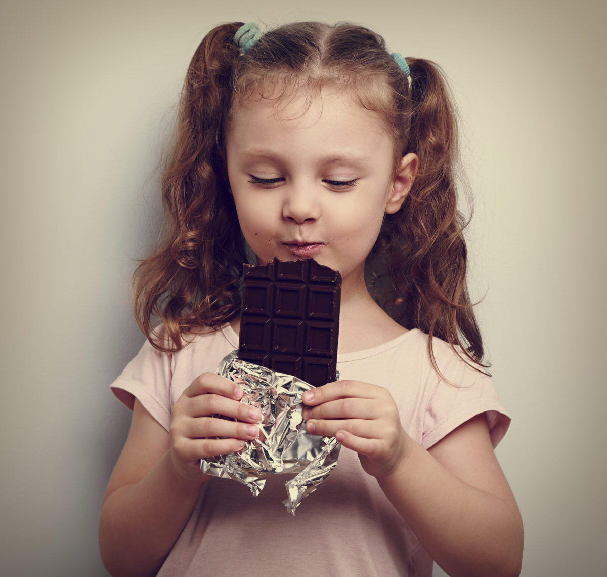 Happy kid girl eating health dark chocolate with pleasure and closed eyes.Vintage portrait