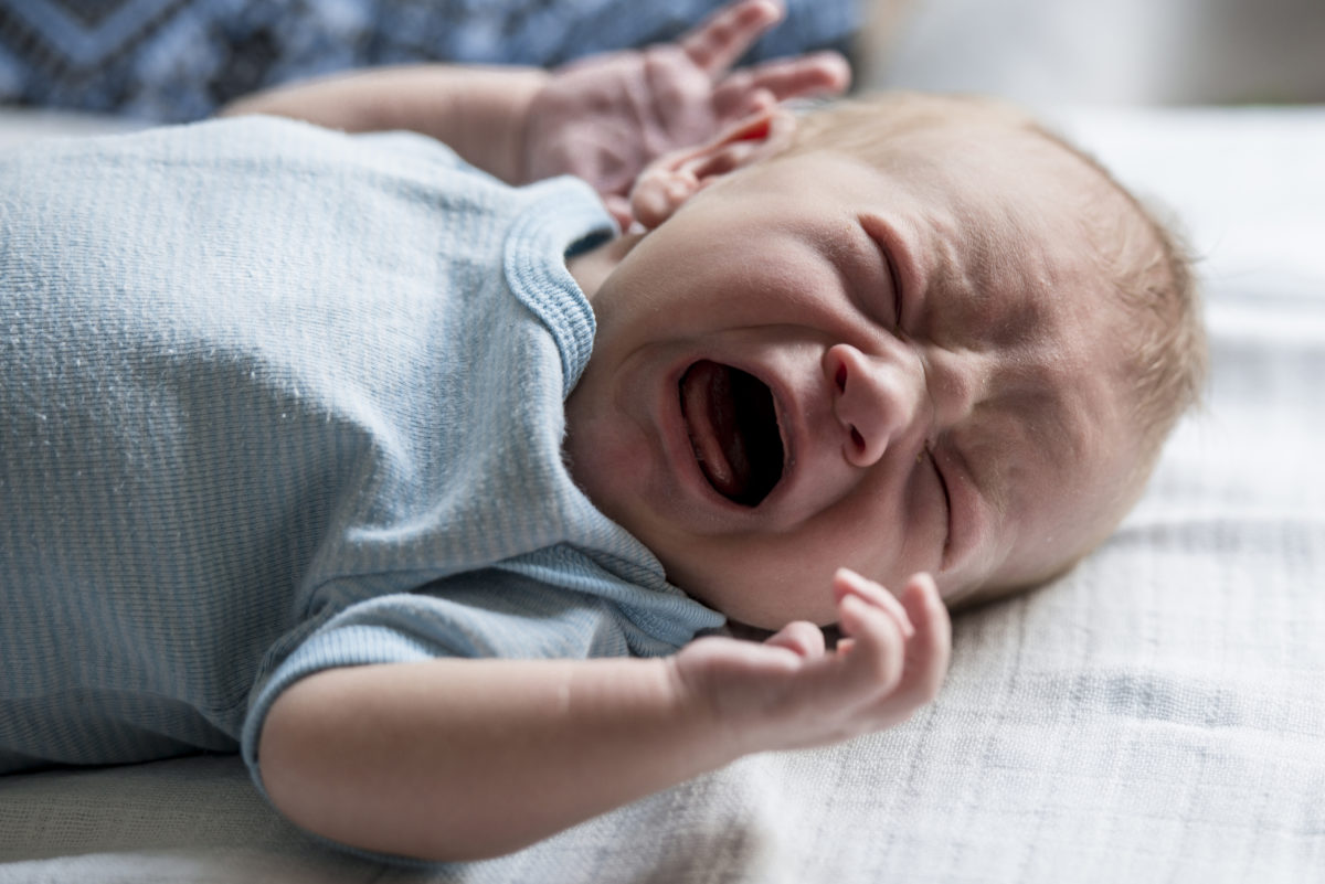 新生婴儿仰卧哭泣。他闭上眼睛，张开嘴。