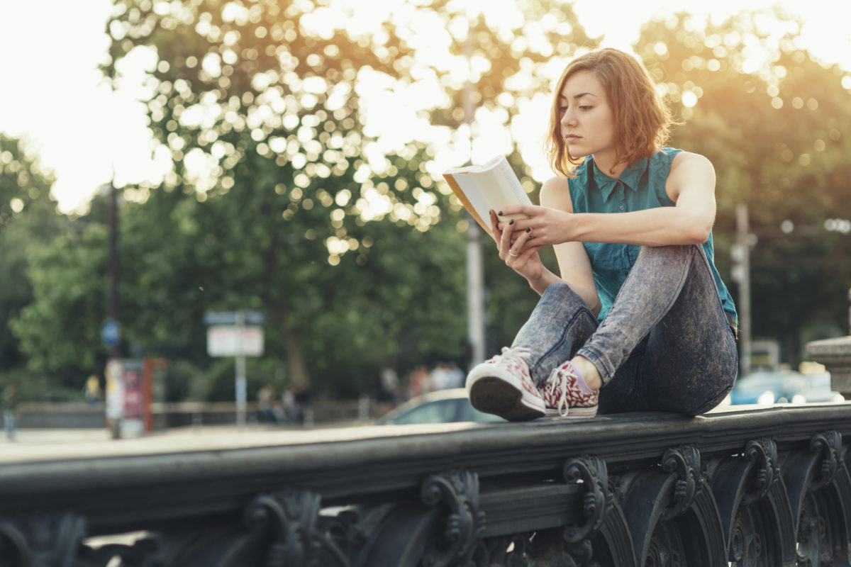 十几岁的女孩坐在大林荫道附近的桥上看书。