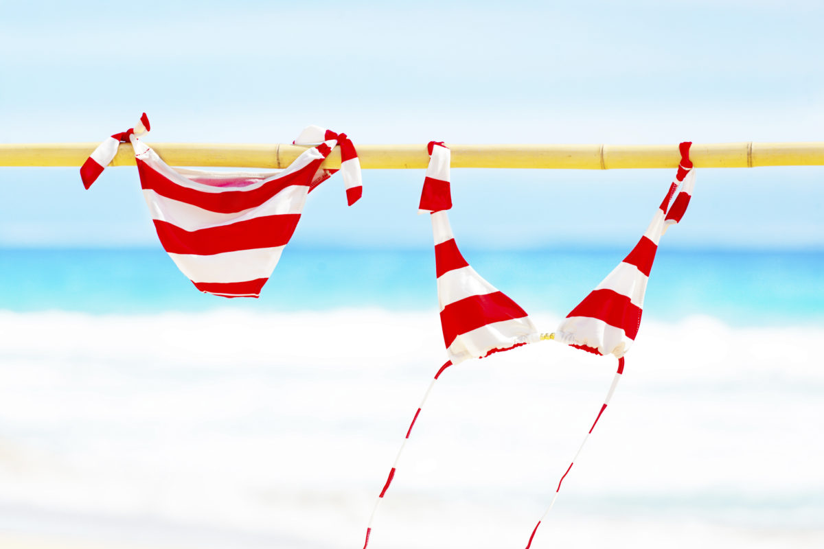 红白相间的比基尼泳装在海边的竹竿上晾晒，阳光明媚。专为旅行而设计，旅游业。在考艾岛拍摄，夏威夷，水平格式，有可用的复印空间。
