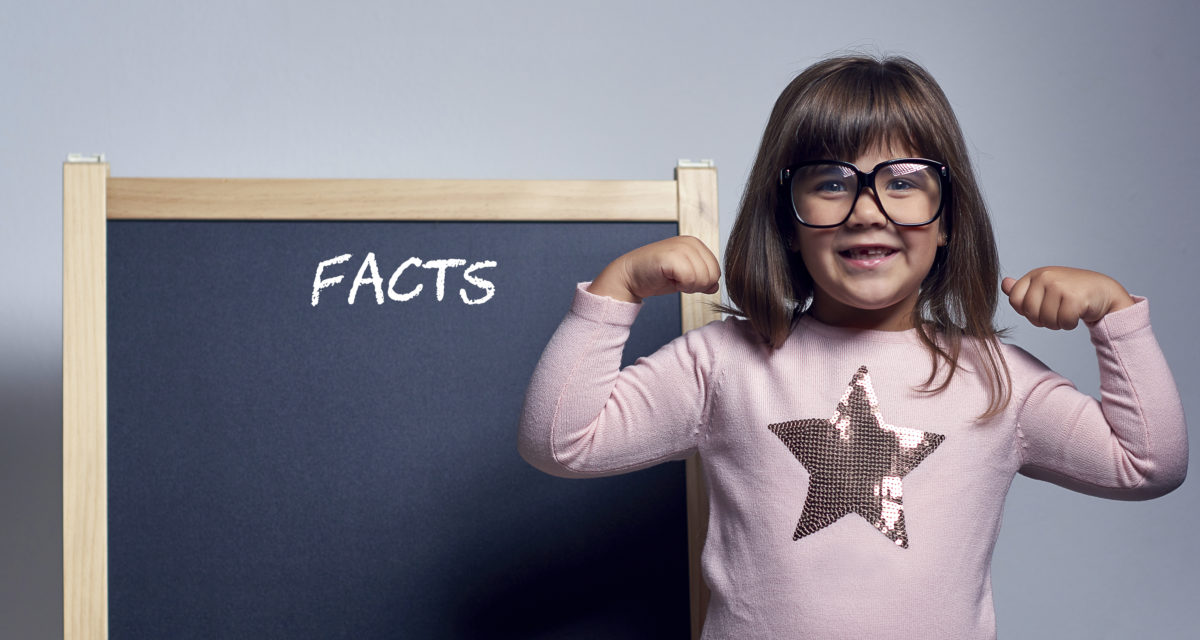 有趣的书呆子女孩的肖像，戴着眼镜，摆姿势，伸展肌肉，在黑板后面摆姿势，上面写着事实。
