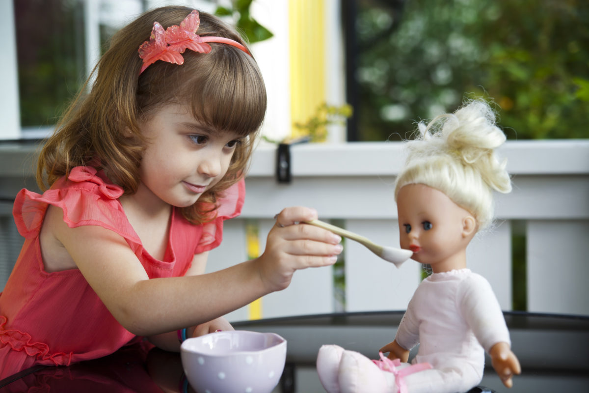 小女孩用勺子喂洋娃娃。
