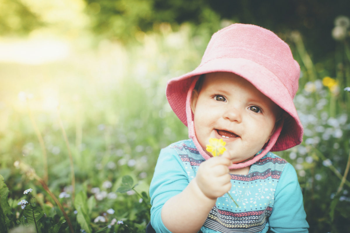 快乐的小女孩坐在草地上，拿着一朵毛茛花。