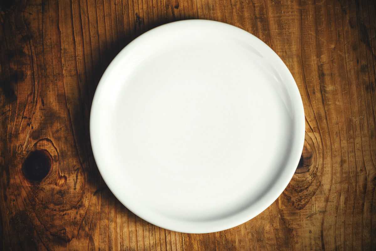 空的白色餐盘放在质朴的木制厨房餐桌上，俯视图