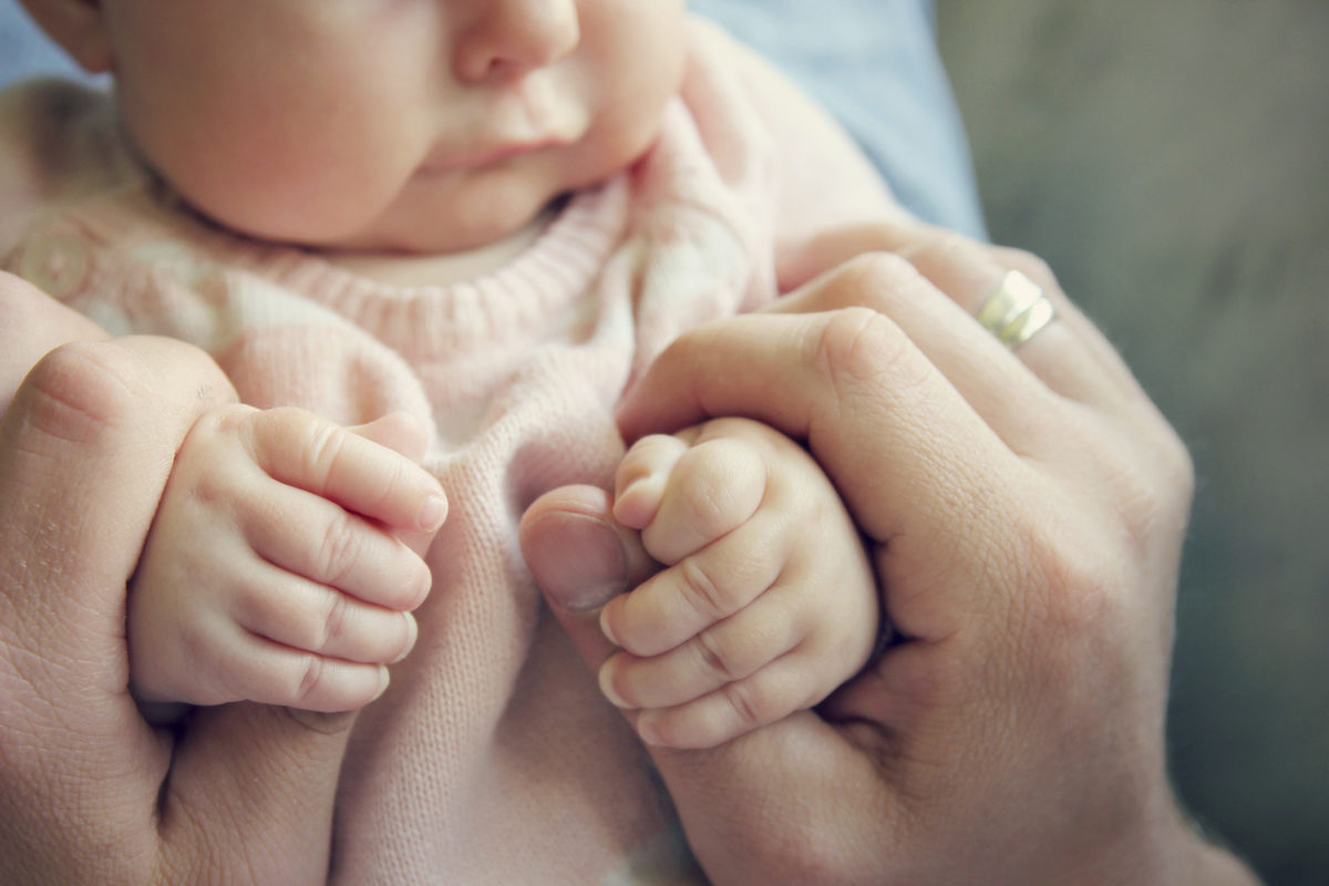 专注于一个3个月大的女婴的手，握住她父亲的手指。复古风格的颜色过滤器。