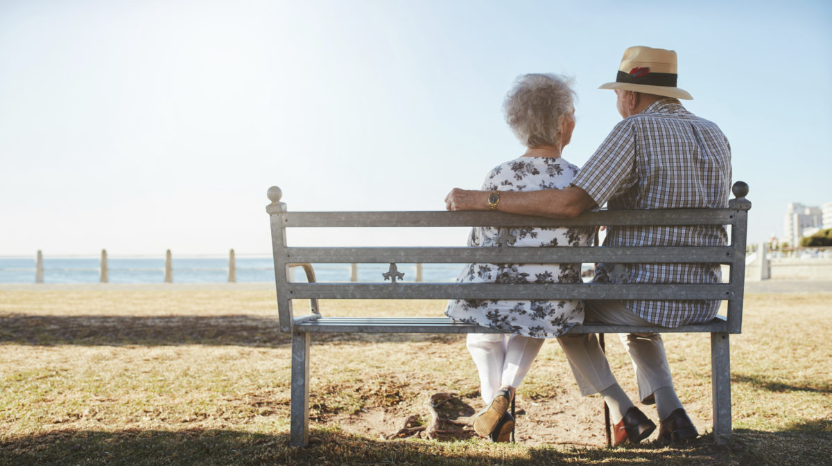 Rear view of loving senior couple relaxing at the seaside.Elderly man and woman sitting a bench outdoors.
