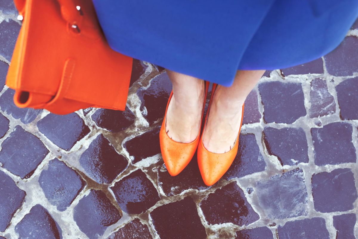 穿橙色鞋子的女人的腿。亮橙色的鞋子和包。警察，橙色经典女鞋和手提包。下雨天。街头时尚。街头风格。商务休闲装。秋装。
