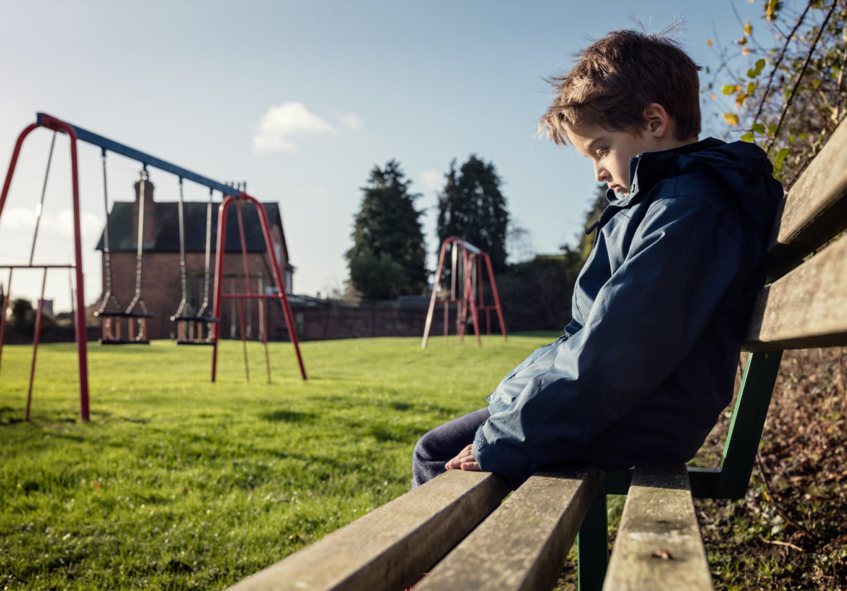 心烦意乱的问题孩子坐在游乐场长椅上欺负孩子，抑郁，儿童保护或孤独