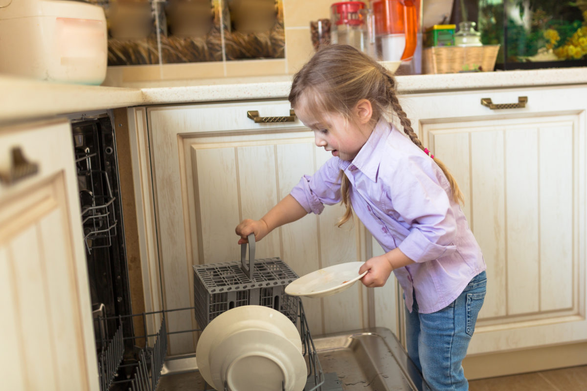 Smiling caucasian girl helping in kitchen taking plates out of dish washing machine,casual lifestyle photo series in real life interior