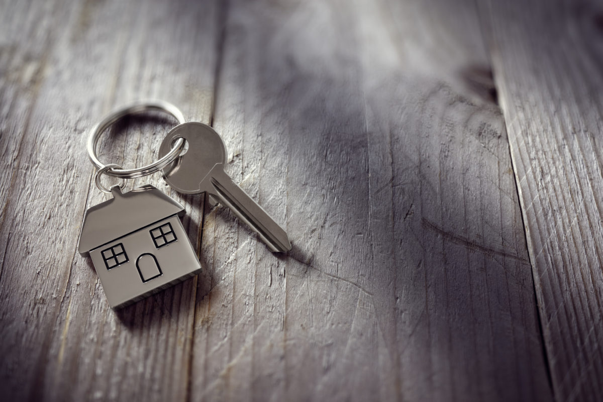 在一个房子形状的钥匙链上的房子钥匙，依靠木地板的概念，用于房地产，搬回家或租房