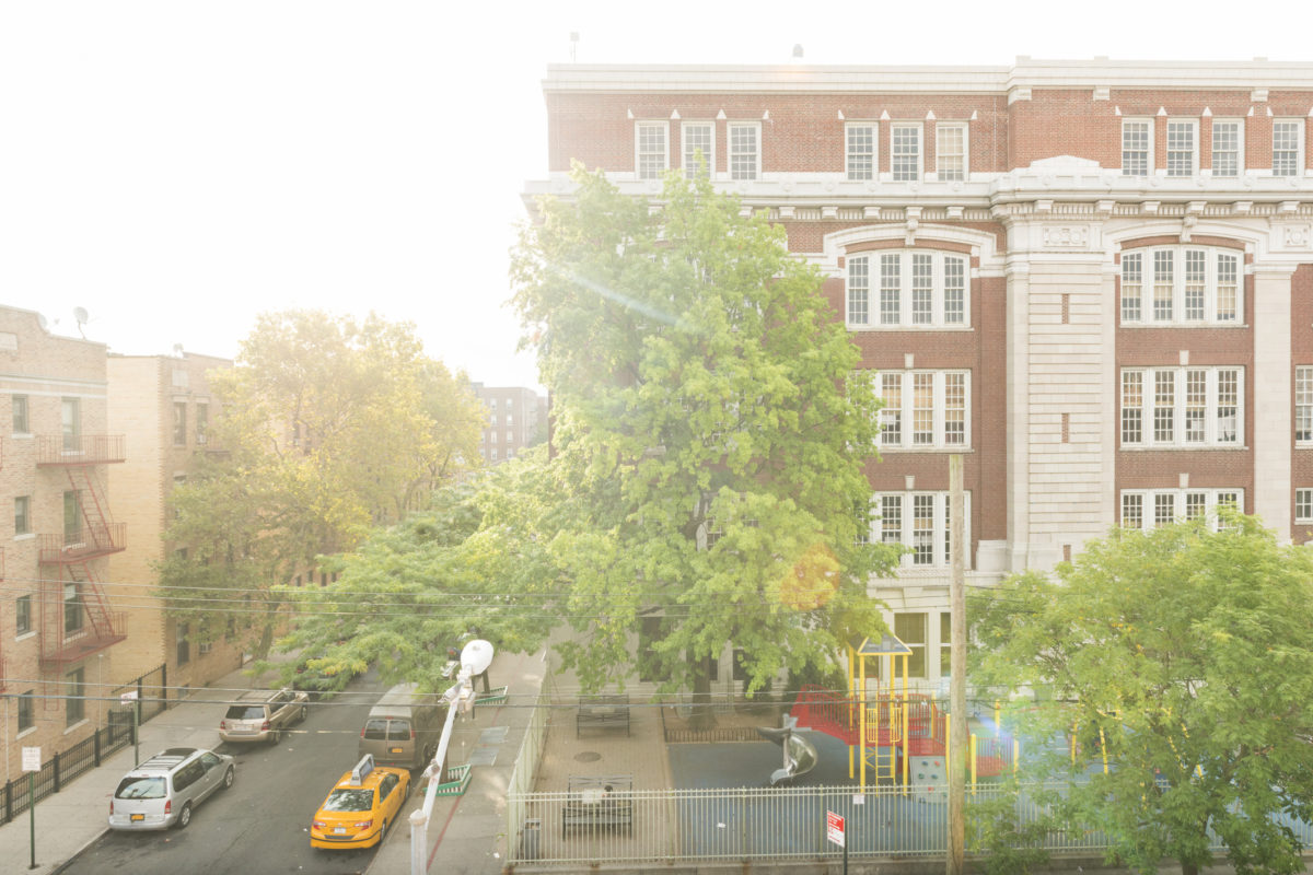 皇后区，美国- 9月18日，2016年:在纽约市埃尔姆赫斯特区，一所小学坐落在一栋多层砖砌建筑中。清晨的阳光照耀着住宅区和街道，街道两旁停满了汽车。