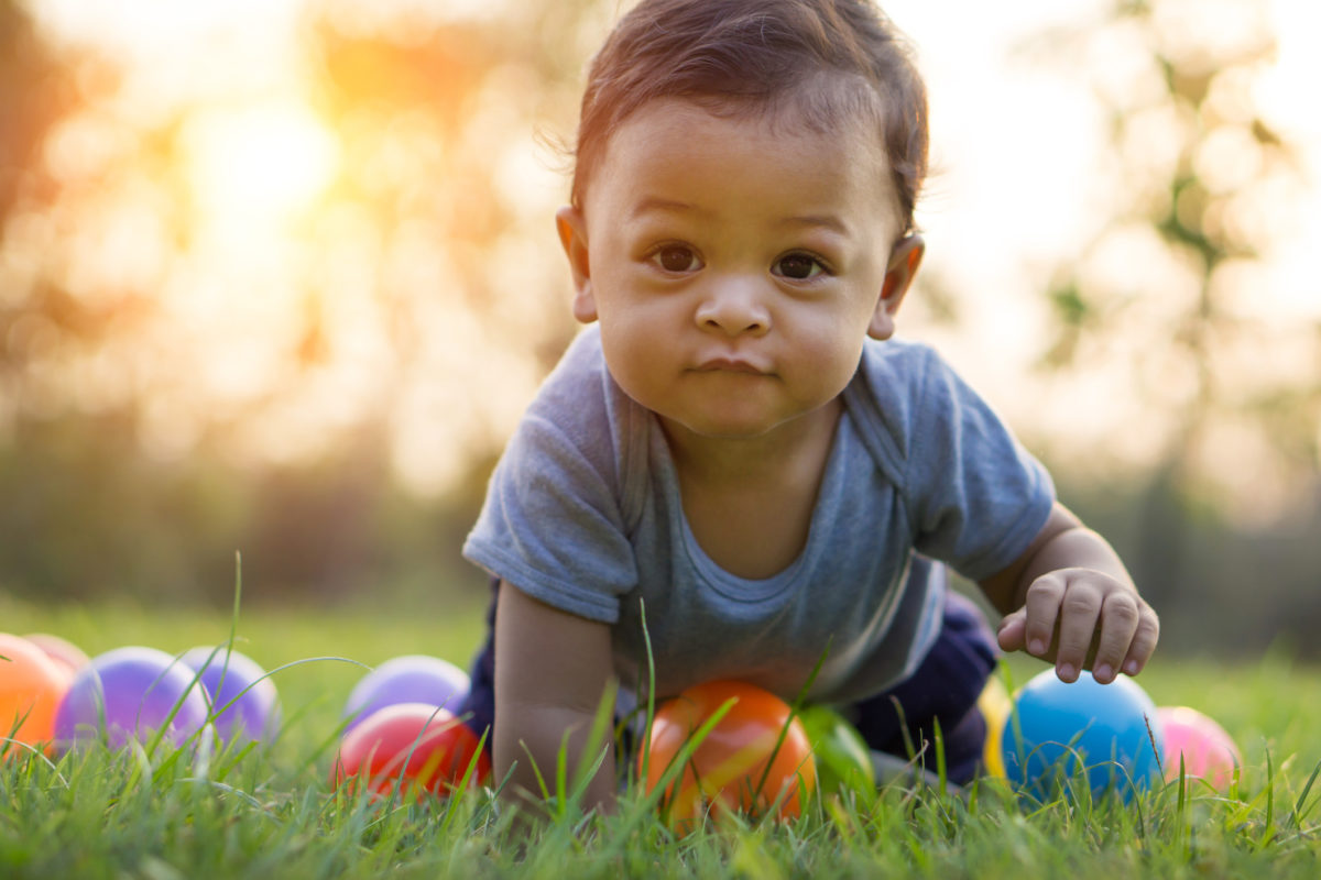 可爱的亚洲宝宝爬在绿草和五颜六色的球-日落过滤效果