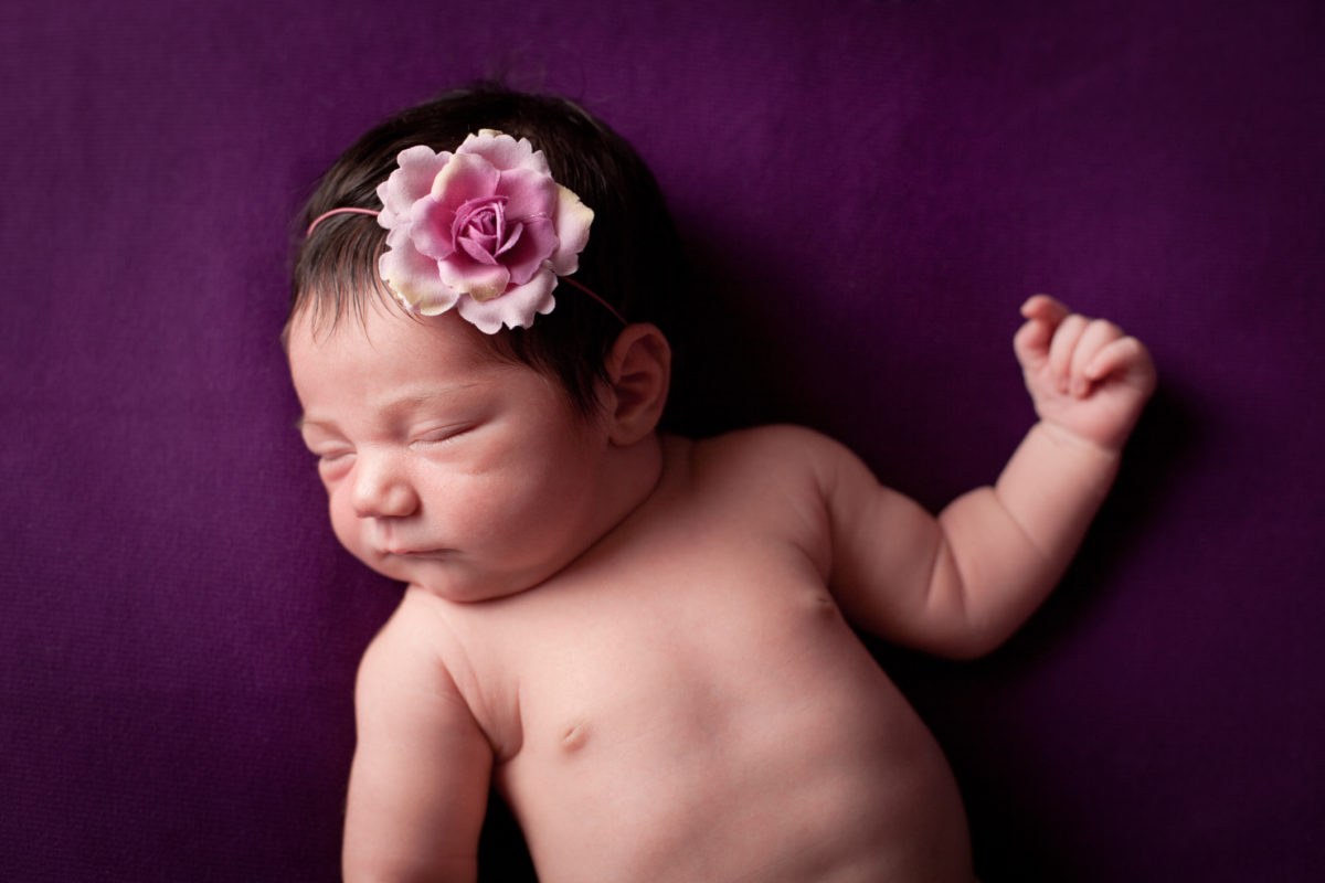 珍贵的彩色图像，新生女婴，戴着花头带，紫色背景。