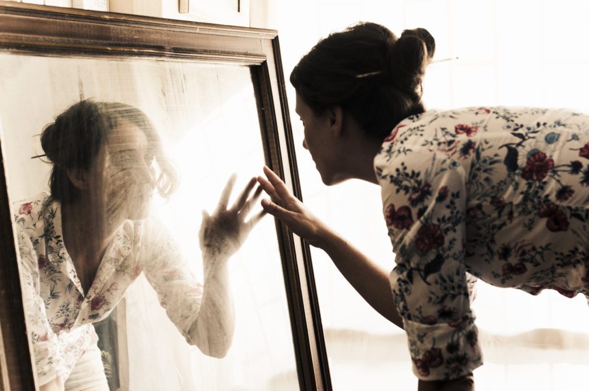艺术家，中年妇女在镜子上看着自己。镜子上的灰尘…