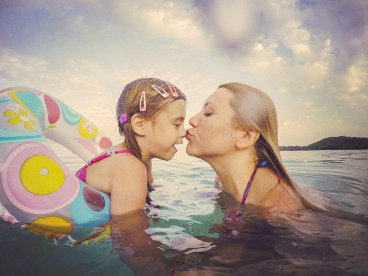母亲和女儿在海里玩得很开心。真正的家庭，真正的情感。水溅到相机上。复古色调。