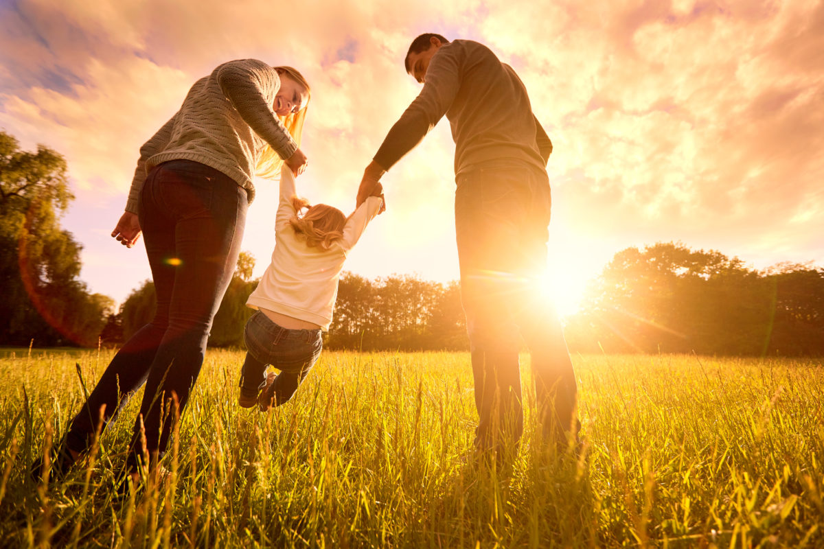 欢乐的家庭在公园的夜光下。太阳光。妈妈，爸爸和宝宝在日落时快乐地散步。幸福家庭的概念。父母牵着孩子的手。
